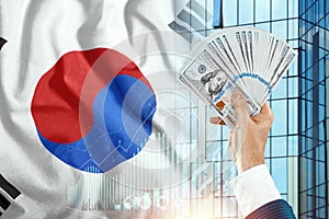 Money in a man`s hand against the background of the flag of South Korea. Income of Koreans. Financial condition of South Koreans,