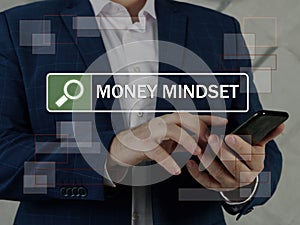 MONEY MINDSET text in search line. Manager looking for something at smartphone. A money mindset is an overriding attitude that