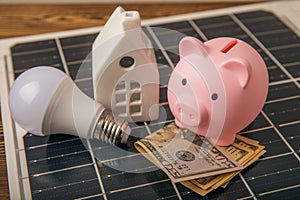 Money, a piggy bank, a LED lamp and a house model on the background of solar panels, close-up.