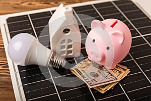 Money, a piggy bank, a LED lamp and a house model on the background of solar panels, close-up.