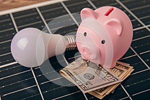 Money, a piggy bank, a LED lamp and a house model on the background of solar panels, close-up.