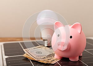 Money, a piggy bank, a LED lamp and a house model on the background of solar panels, close-up.