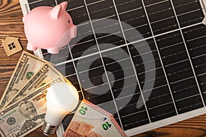 Money, a piggy bank, a LED lamp and a house model on the background of solar panels, close-up.