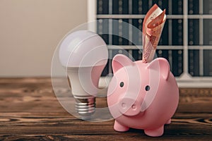 Money, a piggy bank, a LED lamp and a house model on the background of solar panels, close-up.