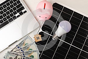 Money, a piggy bank, a LED lamp and a house model on the background of solar panels, close-up