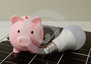 Money, a piggy bank, a LED lamp and a house model on the background of solar panels, close-up