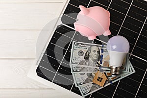 Money, a piggy bank, a LED lamp and a house model on the background of solar panels, close-up