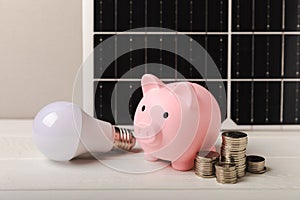 Money, a piggy bank, a LED lamp and a house model on the background of solar panels, close-up
