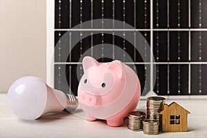 Money, a piggy bank, a LED lamp and a house model on the background of solar panels, close-up