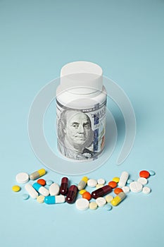 Money and pills of different colors on blue background. Rising cost of health care