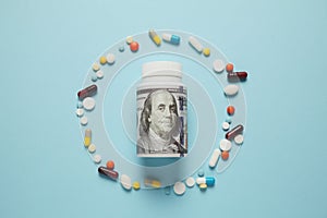 Money and pills of different colors on blue background. Rising cost of health care