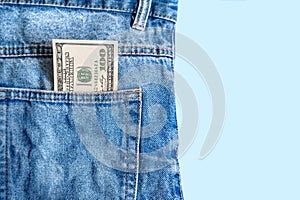 Money in pocket. Banknote of one hundred American dollars in a jeans pocket on a blue background. Copy space. Concept of making