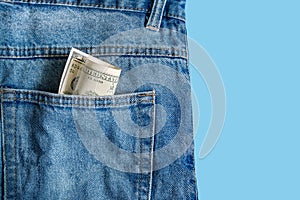 Money in pocket. One hundred American dollars bill in the back pocket of blue jeans on a blue background. Copy space. Concept of