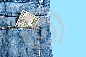 Money in pocket. One hundred American dollars bill in a pocket of blue jeans on a blue background. Copy space. Concept of making