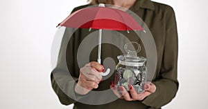 Money protection concept with umbrella over glass jar piggy bank