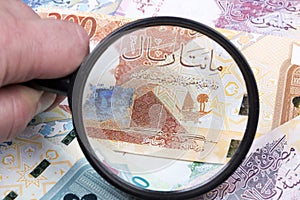 Money from Qatar in a magnifying glass a background