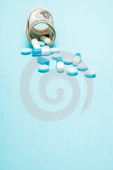 Money rolled up with pills flowing out isolated on blue background, high costs of expensive medication concept. Copy