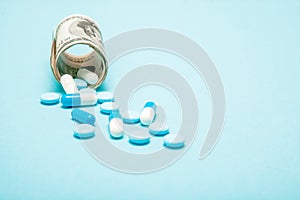 Money rolled up with pills flowing out isolated on blue background, high costs of expensive medication concept. Copy space