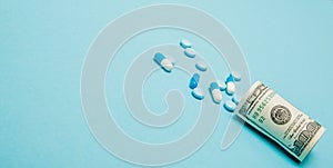 Money rolled up with pills flowing out isolated on blue background, high costs of expensive medication concept. Copy space