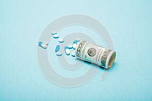 Money rolled up with pills flowing out isolated on blue background, high costs of expensive medication concept. Copy space