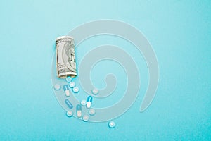 Money rolled up with pills flowing out isolated on blue background, high costs of expensive medication concept. Copy space