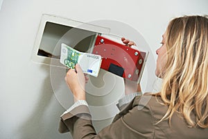 Money safety and security. Woman put savings cash into wall safe