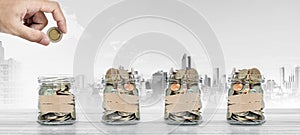 Money saving, Hand putting coin in glass jar with coins inside, with city background