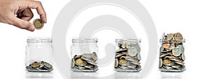 Money saving, Hand putting coin in glass jar with coins inside growing up, on white background photo