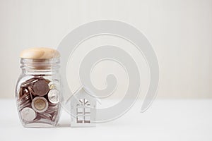 Money of savings coins in glass jar with model white house on wooden table. Property investment and house mortgage financial