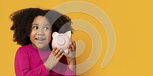 Money Savings. Cute Little Black Girl Holding Piggy Bank Near Ear