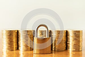 Money and Security Concept. Closeup of golden master key lock with stack of gold coins on wooden table