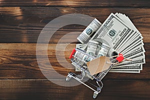 Money in a small supermarket trolley with price tag on old wooden background. Money business finance