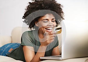 Money spent well. a woman using her laptop on the sofa at home while holding a bankcard. photo