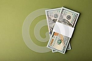 Money, stacks of US hundred dollar bills on an olive background.