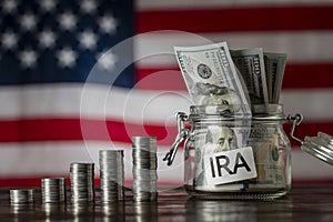 Money towers and glass jar used for saving US dollar bills and notes for IRA retirement fund on the American flag background,