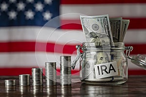 Money towers and glass jar used for saving US dollar bills and notes for IRA retirement fund on the American flag background,