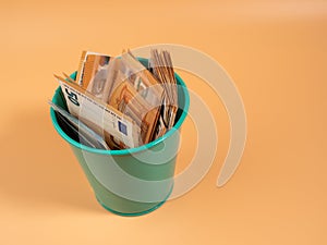 Money in the trash can on an orange background. Euros in the trash. Waste of money concept.