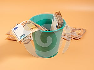 Money in the trash can on an orange background. Euros in the trash. Waste of money concept.