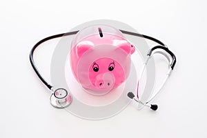 Money for treatment. Medical expenses. Moneybox in shape of pig near stethoscope on white background