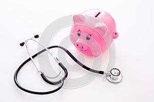 Money for treatment. Medical expenses. Moneybox in shape of pig near stethoscope on white background