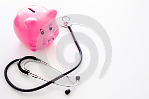 Money for treatment. Medical expenses. Moneybox in shape of pig near stethoscope on white background copy space