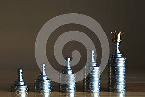 Money is a true king. Chess pawn stand on the highest coin stack wearing a crown. Wealthiness concept