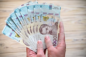 Money of Ukraine. Stack of ukrainian hryvnia banknotes in hands on wooden table. Hryvnia 1000 uah