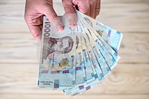 Money of Ukraine. Stack of ukrainian hryvnia banknotes in hands on wooden table. Hryvnia 1000 uah