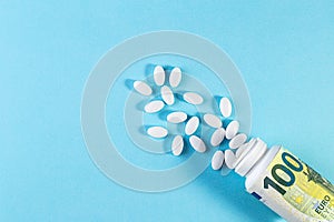 Money and white pills on blue background. Rising cost of health care