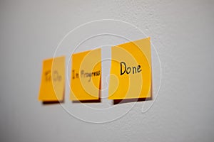 Monitor task of work concept, To do, In progress, Done Note reminder yellow sticker or post note on a white wall close up,.