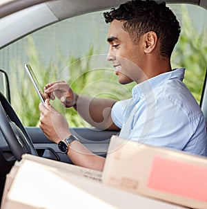 Monitoring it all on his digital system. Shot of a young delivery man using a digital tablet while sitting in a van.