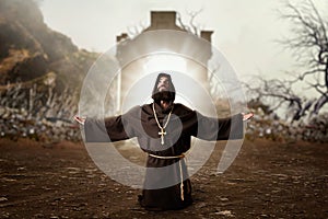 Monk in black robe with hood kneeling and praying