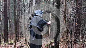 A monk in a black robe walks with a staff through the forest, a wandering druid in a cassock makes his way through the thickets.