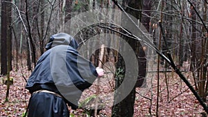 A monk in a black robe walks with a staff through the forest, a wandering druid in a cassock makes his way through the thickets.